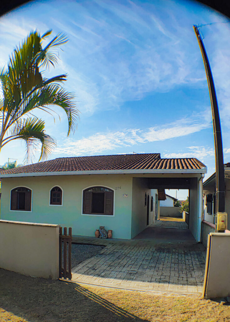 Casa com 3 quartos, na cor verde com palmeira e céu azul em Itapoá - SC