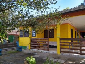 Casa na beira do rio Saí-Mirim em Itapoá, com pintura amarela e vegetação verde.