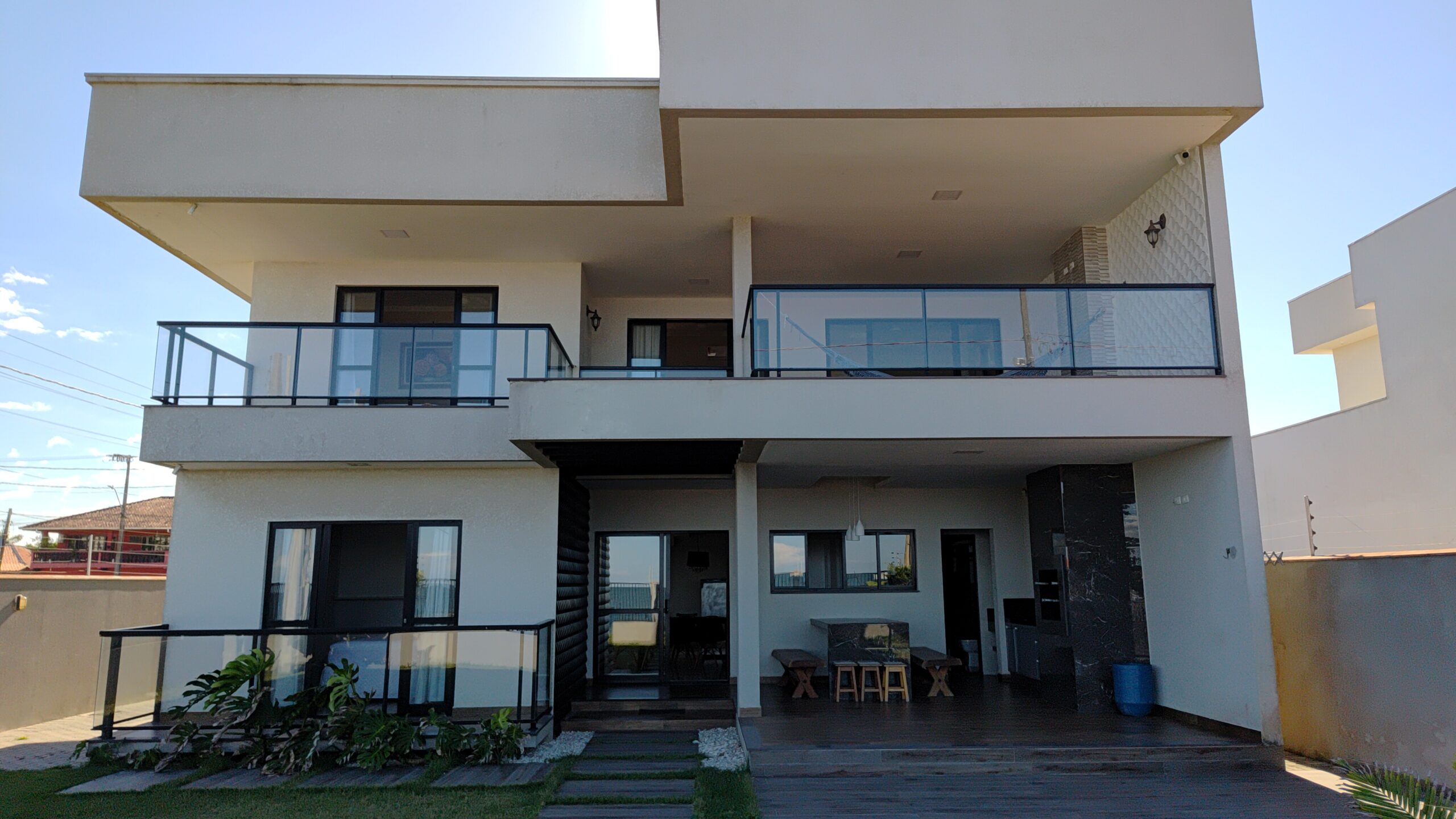 Sobrado em frente ao mar com acabamento moderno, portas e janelas de vidro com área coberta com churrasqueira e grande jardim gramado.