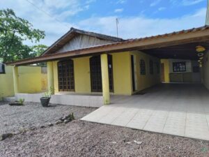 Casa a 300 metros da praia com fachada amarela e garagem com churrasqueira.